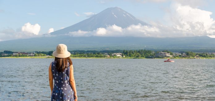 woman in blue dress with hat seeing Mountain Fuji in summer.