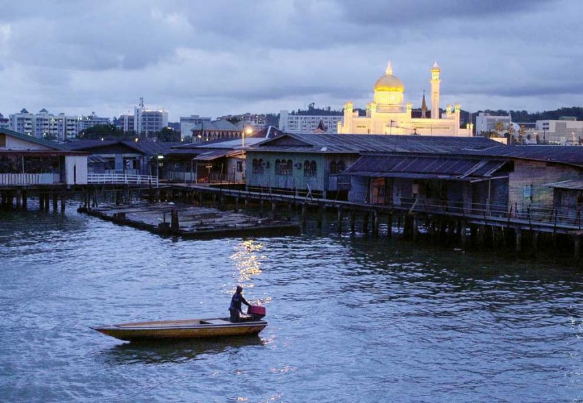 A boat passes through the Kampong Ayer water village at dusk as the Sultan Omar ‘