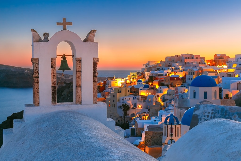 Arch-with-a-bell-white-houses-and-church-with-blue-domes-in-Oia-or-Ia-at-sunset-island-Santorini-Greece-min